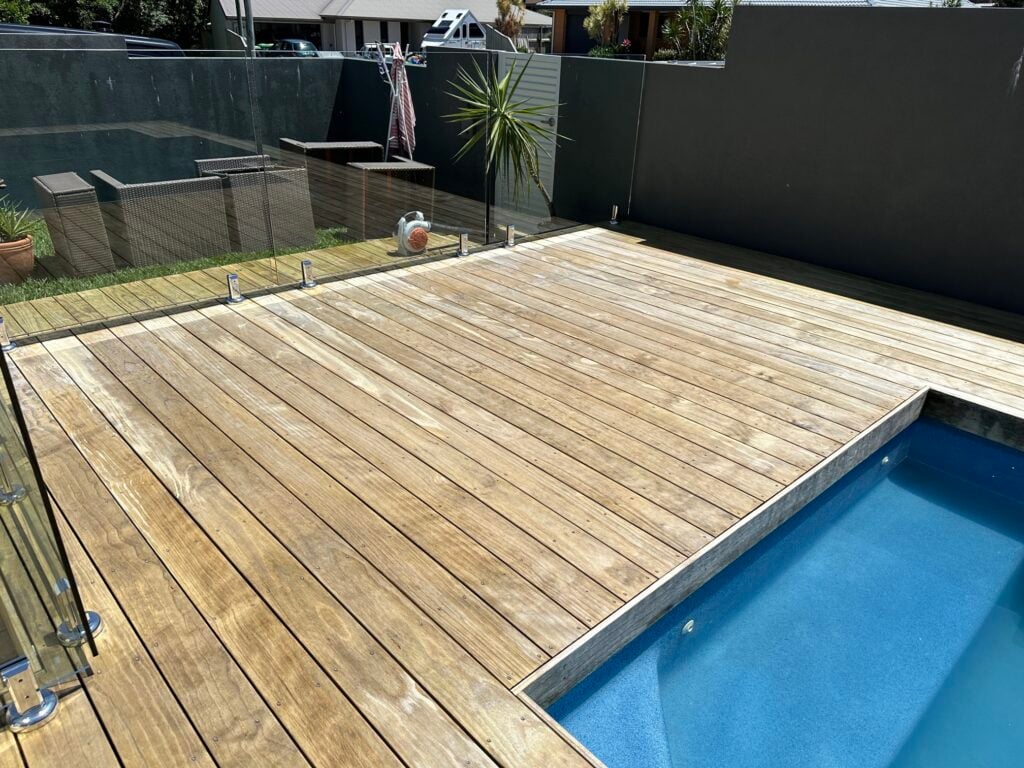 high-pressure cleaned wooden deck with a glass railing overlooking a swimming pool