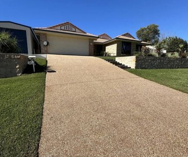 residential driveway made of exposed aggregate concrete. The driveway slopes upward towards a two-story house with a garage.